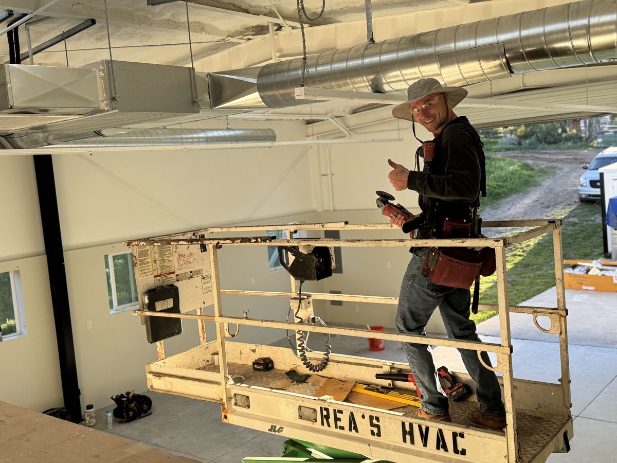 Rea's HVAC crew on scissor lift beneath custom cross-broken sheet-metal plenum, square-to-round transition, and spiral trunk