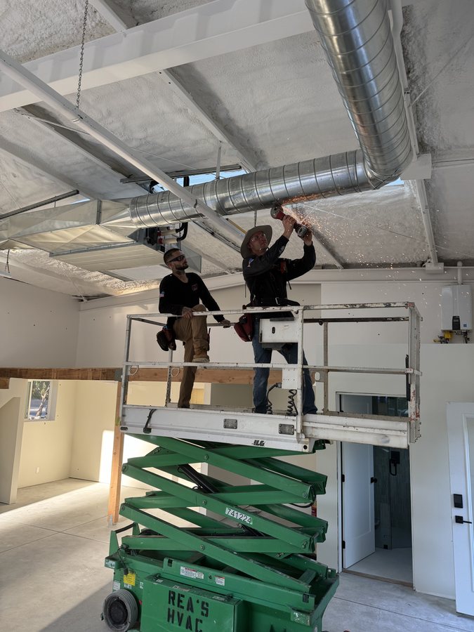 In-house sheet-metal installers cutting overhead spiral galvanized duct on a Rea's HVAC scissor lift